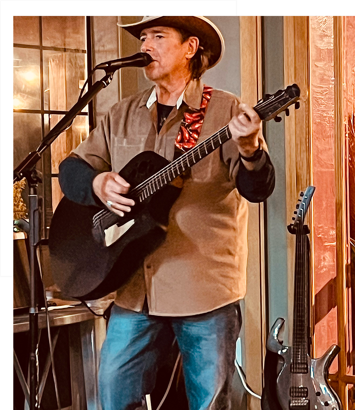 A man in a cowboy hat plays guitar and sings indoors.