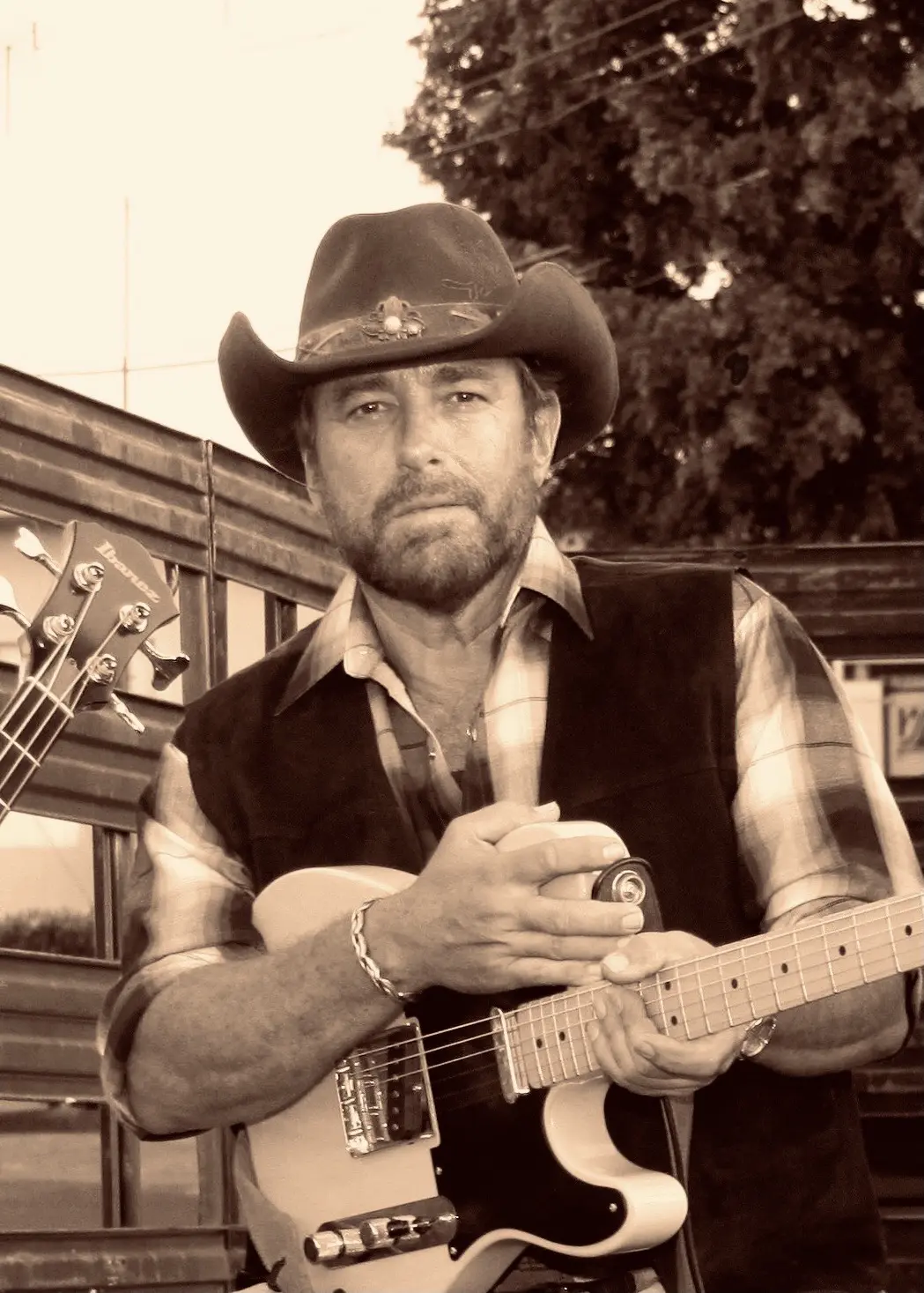 Man in cowboy hat playing electric guitar outdoors.