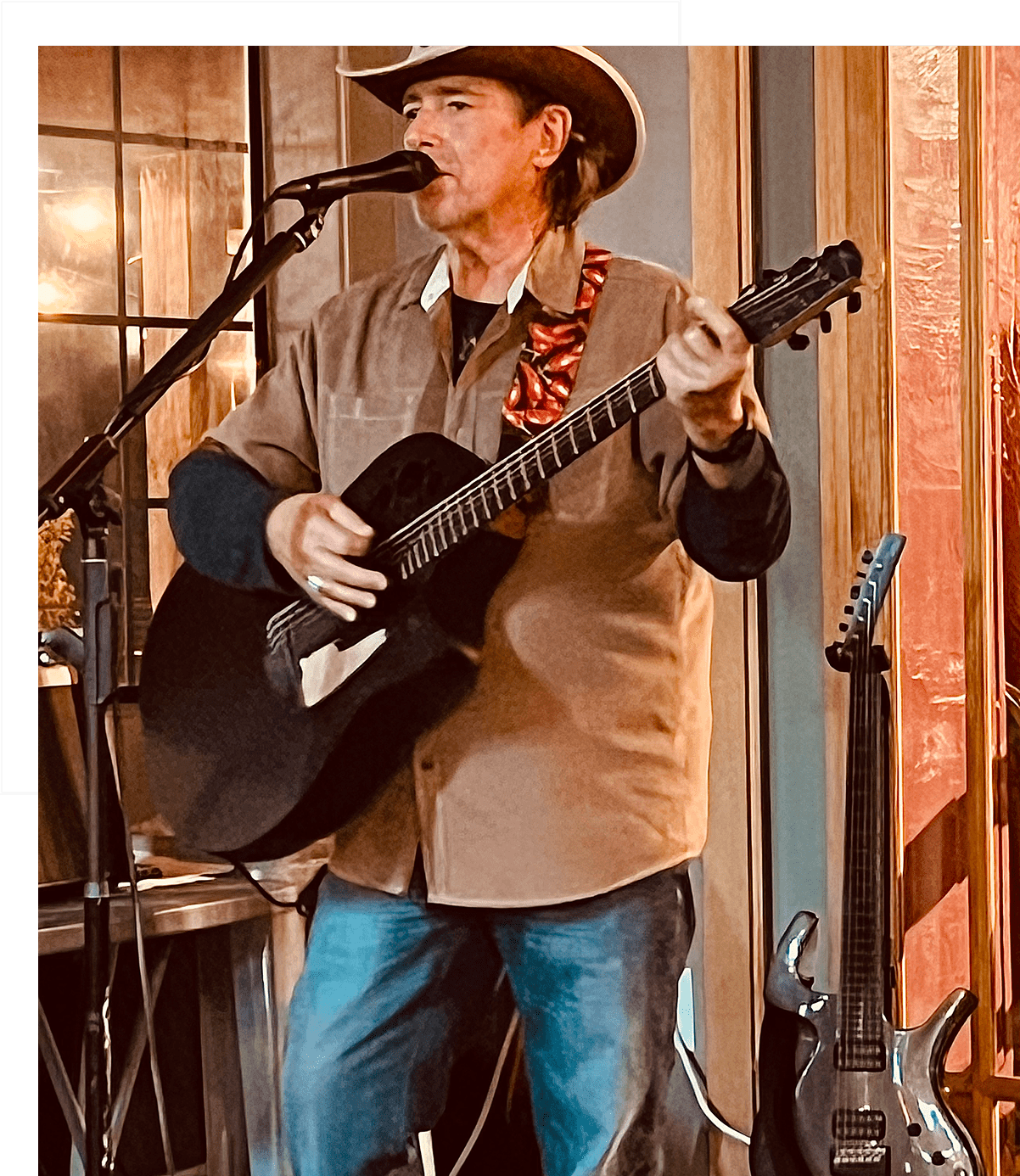 A man in a cowboy hat plays guitar and sings indoors.
